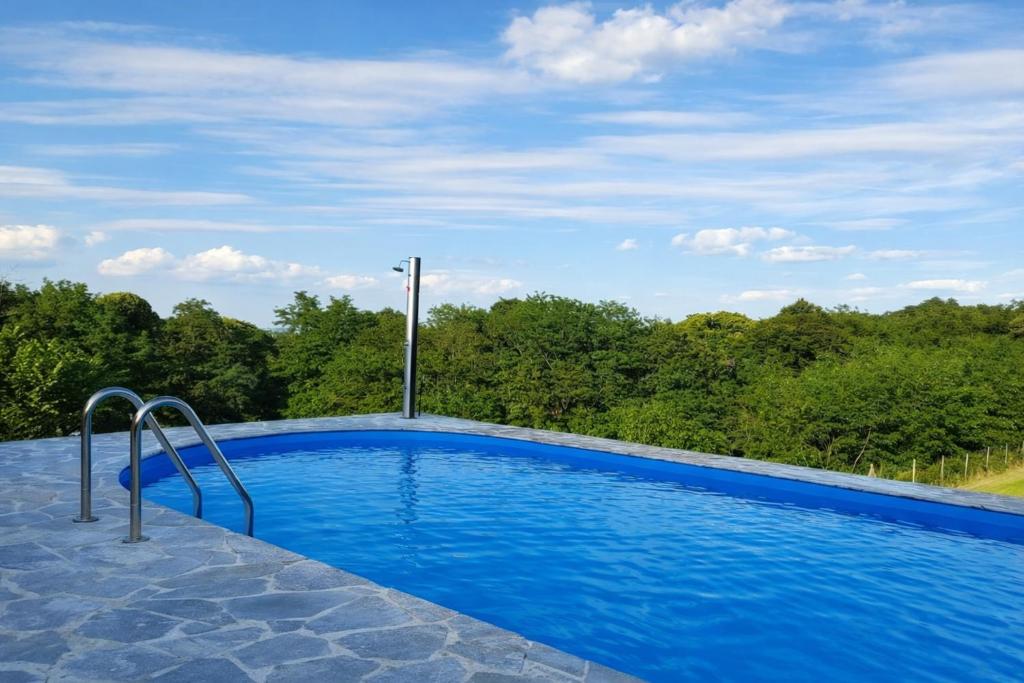 a blue swimming pool with trees in the background at Family Retreat with Pool, BBQ & Green Escape by Destination GREEN Croatia in Praporčan