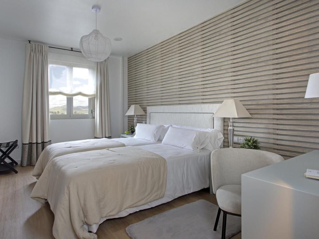 a white bedroom with a large bed and a chair at Hotel Faisanera Golf in Palazuelos de Eresma