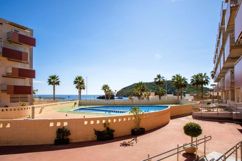 a resort with a pool and palm trees and the ocean at Apto Primera Línea con Piscina - Guipas Beach in Puerto de Mazarrón