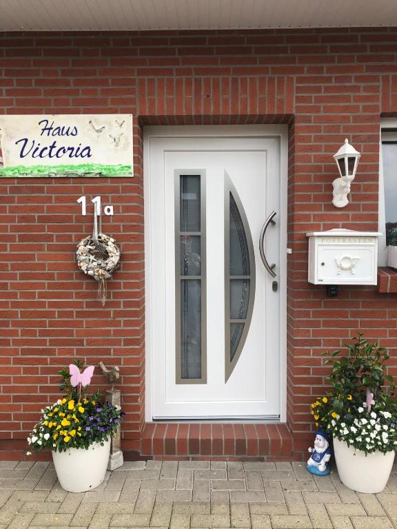 a white door on a brick building with two plants at Ferienhaus Victoria in Norden