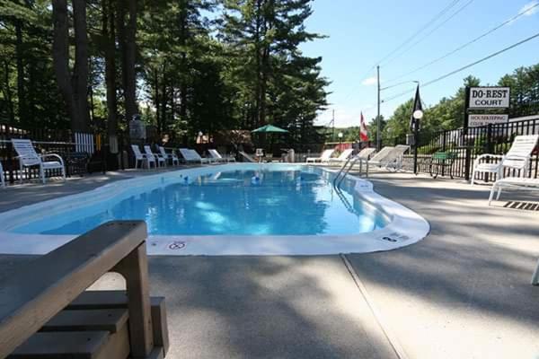a large swimming pool with white chairs and chairs at Do-Rest Court in Lake George