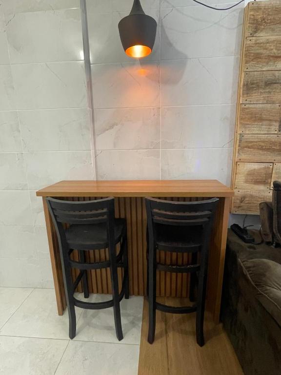 a wooden table with two black chairs under it at Som do mar Kitinete in São Vicente