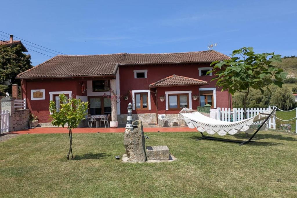 a red house with a hammock in a yard at Casa de campo La Casuca Del Monje, San Vicente de la Barquera in La Acebosa