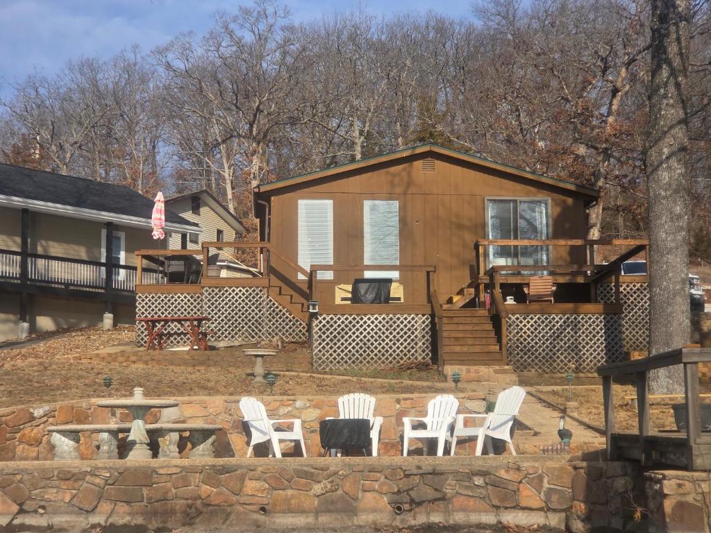 a wooden cabin with white chairs and a table and a firepit at Shady Valley Lakefront Cottage in Sunrise Beach