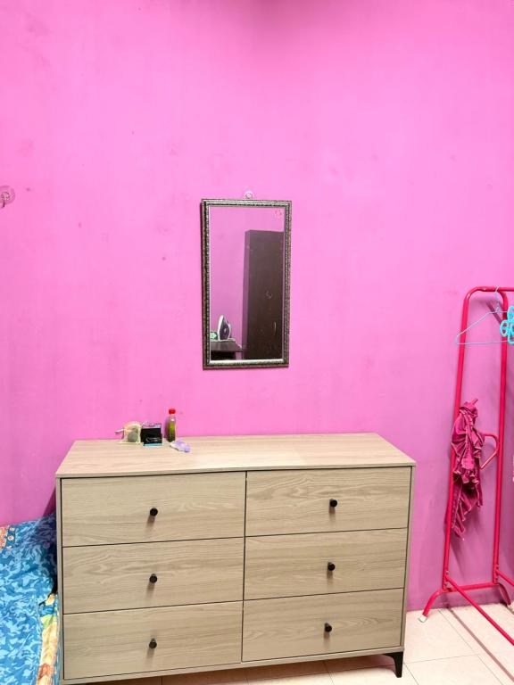 a dresser with a mirror on a pink wall at Homestay Arich in Permatang Pauh