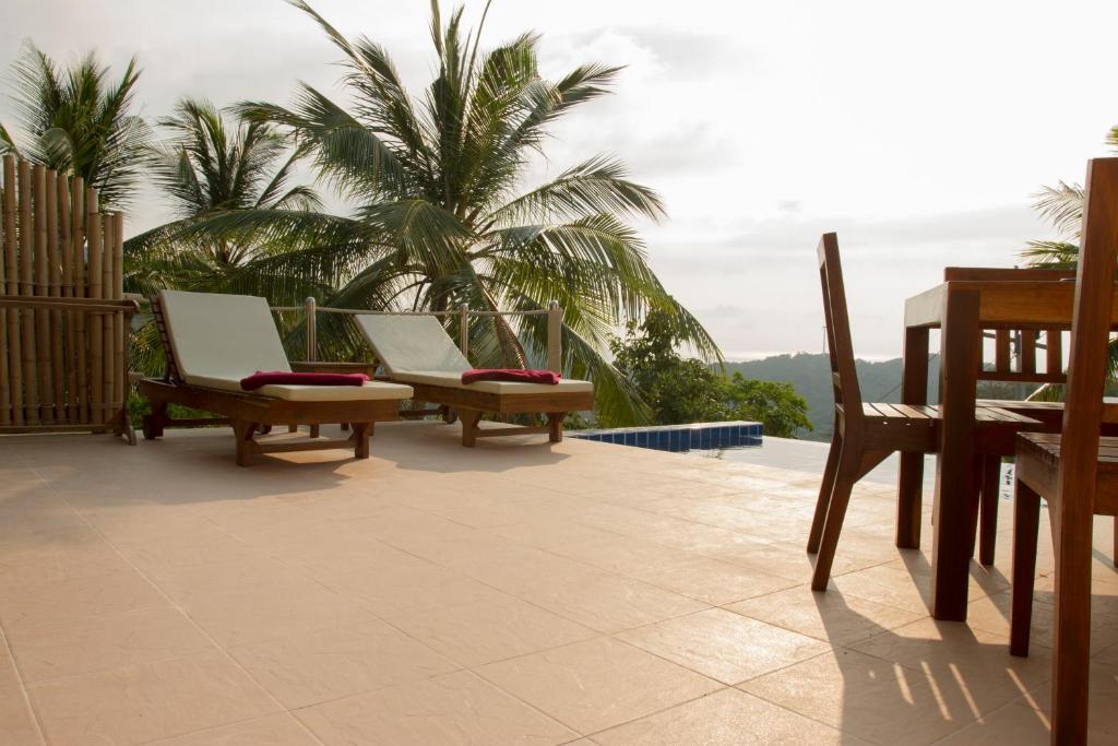 a patio with two chairs and palm trees in the background at Karo Villas in Koh Tao