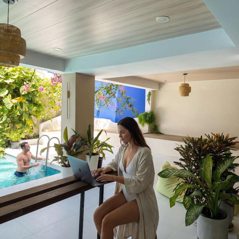a woman sitting on a table with a laptop in front of a pool at Kue Hotel Maafushi in Maafushi