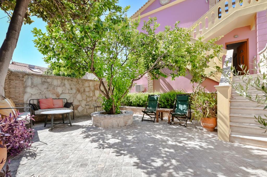 a patio in front of a pink house with chairs and a tree at Citron, Parga Center Residence in Parga