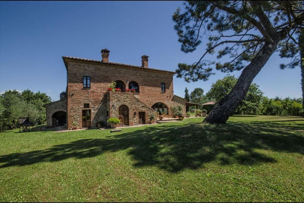 un grand bâtiment en briques avec un arbre dans la cour dans l'établissement Villa Scianellone, à Torrita di Siena