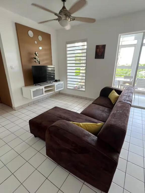 a living room with a brown couch and a flat screen tv at Appartement tout confort et idéalement situé in Petit-Bourg