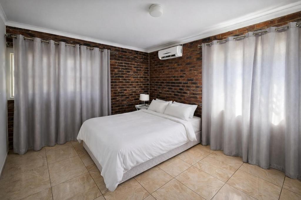 a bedroom with a white bed and a brick wall at Work, Rest, Repeat, Comfortable 2BR Flat in Kathu in Kathu