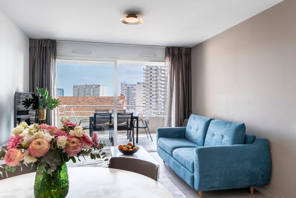 a living room with a blue couch and a table with flowers at Victoria Palace- l'appartement avec vue mer et à proximité de Monaco in Beausoleil