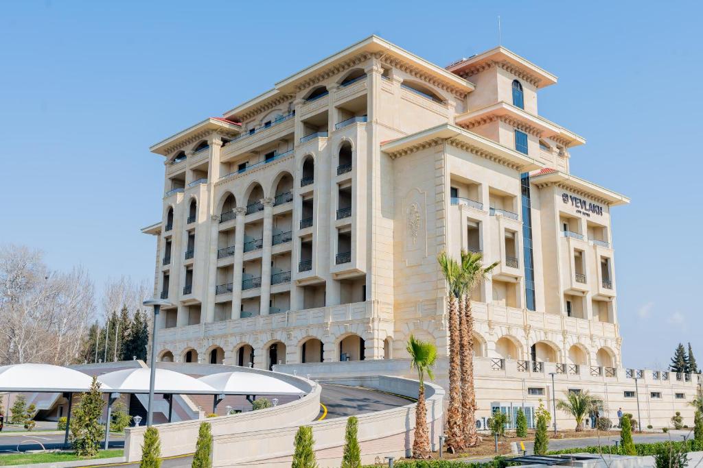 a large building with palm trees in front of it at Yevlakh City Hotel in Yevlax