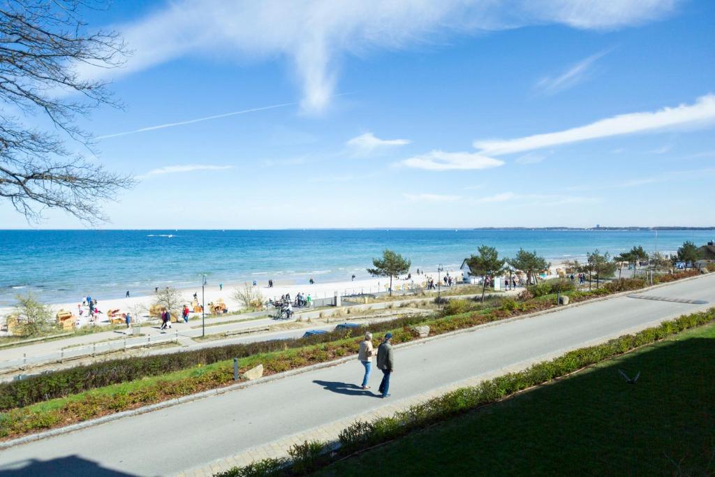 two people walking down a road next to the beach at Ostseeblick Apartment 2 in Scharbeutz