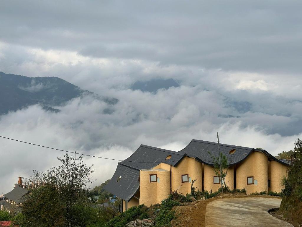 a house on a hill with clouds in the background at Phỏng Lài Mountain Homestay - Ta Xua Peak View in Bắc Yên