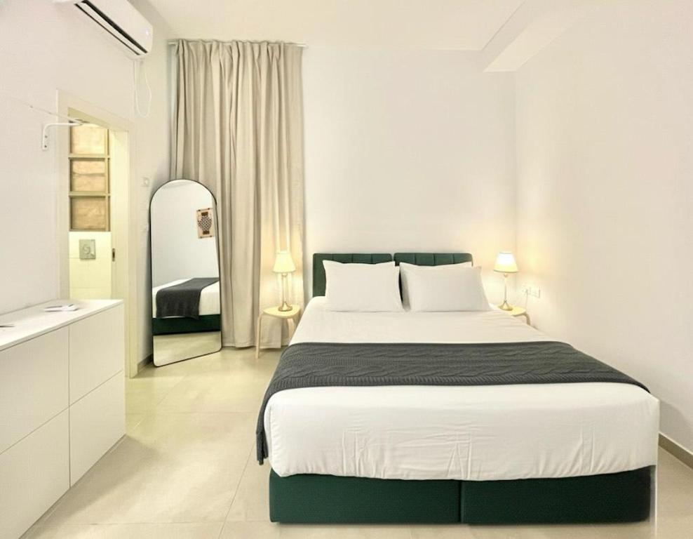 a white bedroom with a large bed and a mirror at Nachlaot Gem - Bright, Central and Cozy in Jerusalem