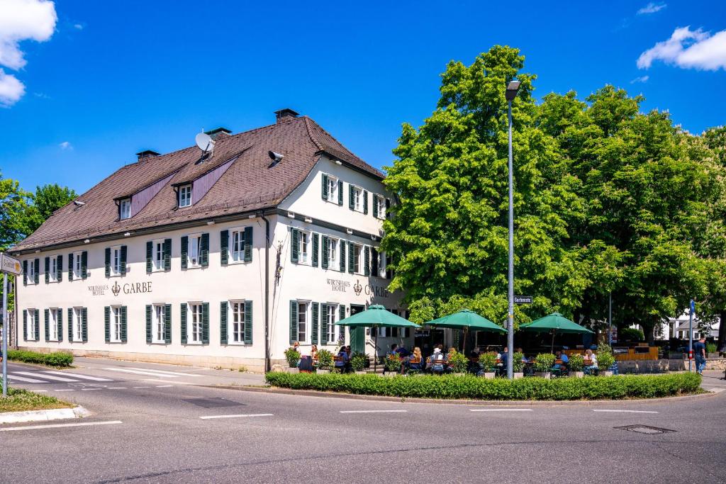 a large white building with tables and green umbrellas at Hotel Wirtshaus Garbe in Stuttgart