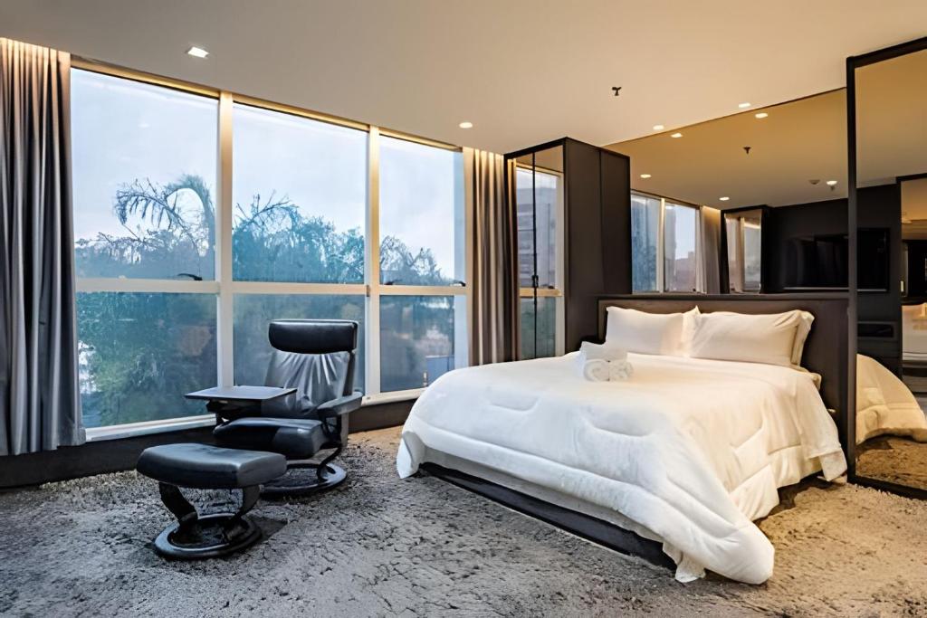 a bedroom with a bed and a chair and windows at Flat moderno Jade hotel in Brasília