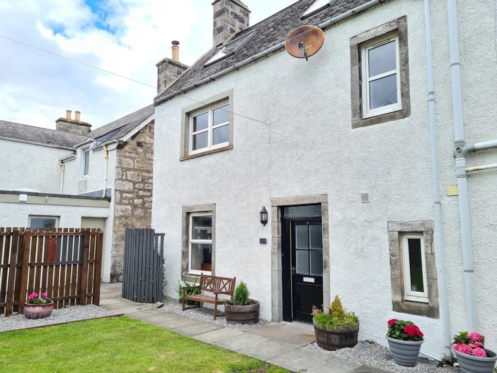 a white brick house with a bench in the yard at The Old Library, Brora in Brora
