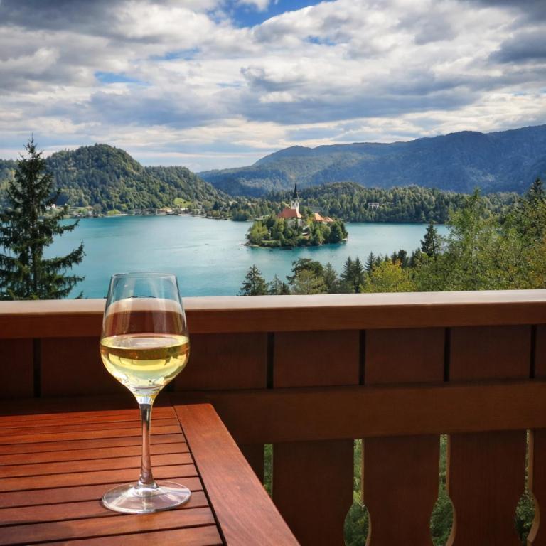 a glass of wine sitting on a table with a view of a lake at Apartment Milly in Bled