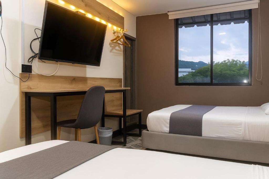 a hotel room with two beds and a desk with a television at Hotel AirPort Pereira in Pereira