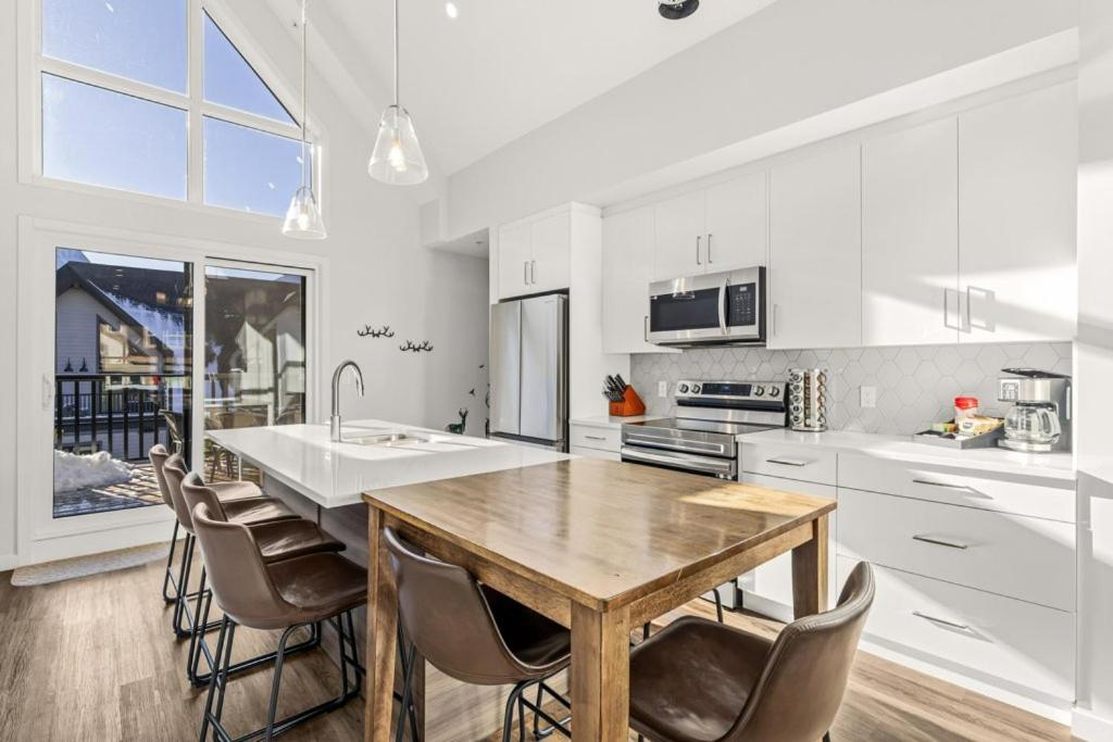 a white kitchen with a wooden table and chairs at Cloudline Vista 3 BdrmTownhouse w Private Garage Views Pool Walk Downtown in Canmore