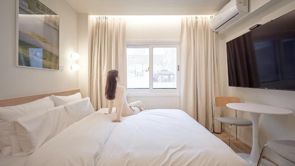 a woman sitting on a bed looking out the window at Maison de Centum Busan in Busan