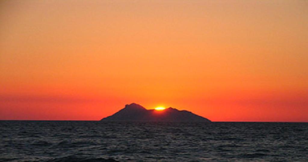 una puesta de sol sobre una pequeña isla en el océano en Artemis Appartments, en Pitsidia