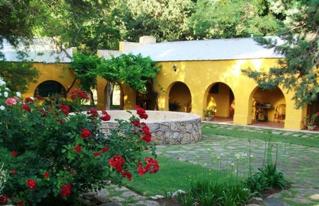 ein gelbes Gebäude mit einem Hof mit roten Blumen in der Unterkunft Hotel de Montaña Estancia Niña Paula in Nono