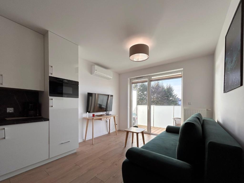 a living room with a green couch and a kitchen at Posesja Kapitańska Apartament 18B 17 przy plaży in Grzybowo