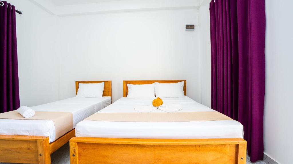 two beds in a room with purple curtains at Near Town Lodge in Dambulla
