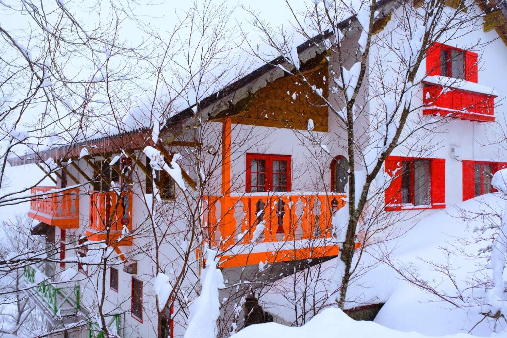 a building with red windows and a balcony in the snow at Winterfell Hakuba in Hakuba