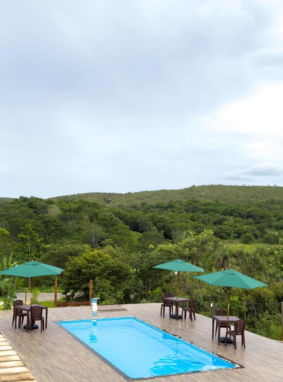 a swimming pool with tables and chairs and umbrellas at Chalé portal da serra in Serra do Cipo