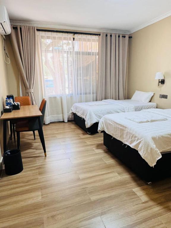 a hotel room with two beds and a desk and a window at Cactus Hotel in Dar es Salaam