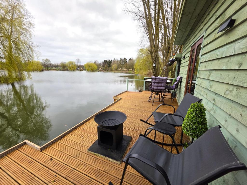 a wooden deck with chairs and a grill next to a lake at The Hideaway Pod in Chelmsford