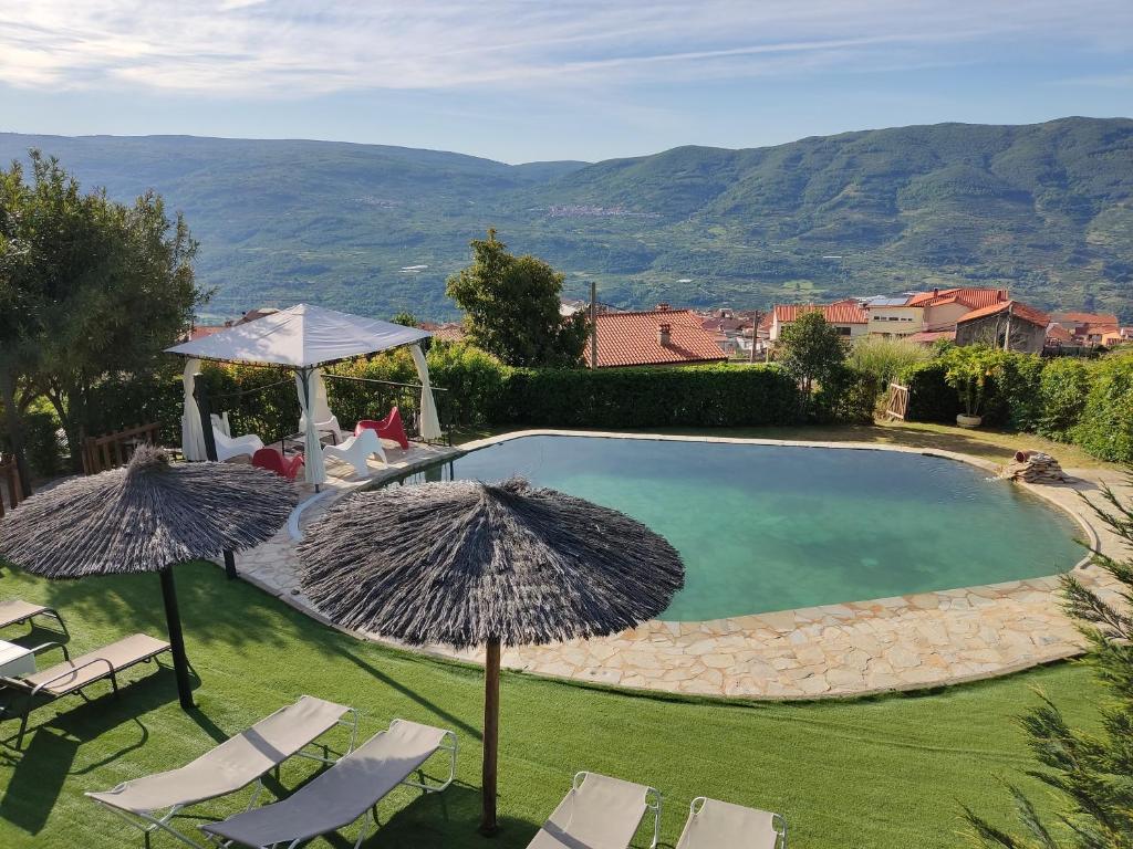 a swimming pool with chairs and umbrellas at Casa Rural El Regajo Valle del Jerte in El Torno