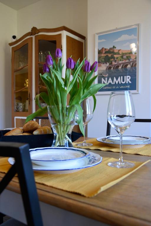 a table with a vase of purple tulips and two wine glasses at La maison du bienvenu in Namur