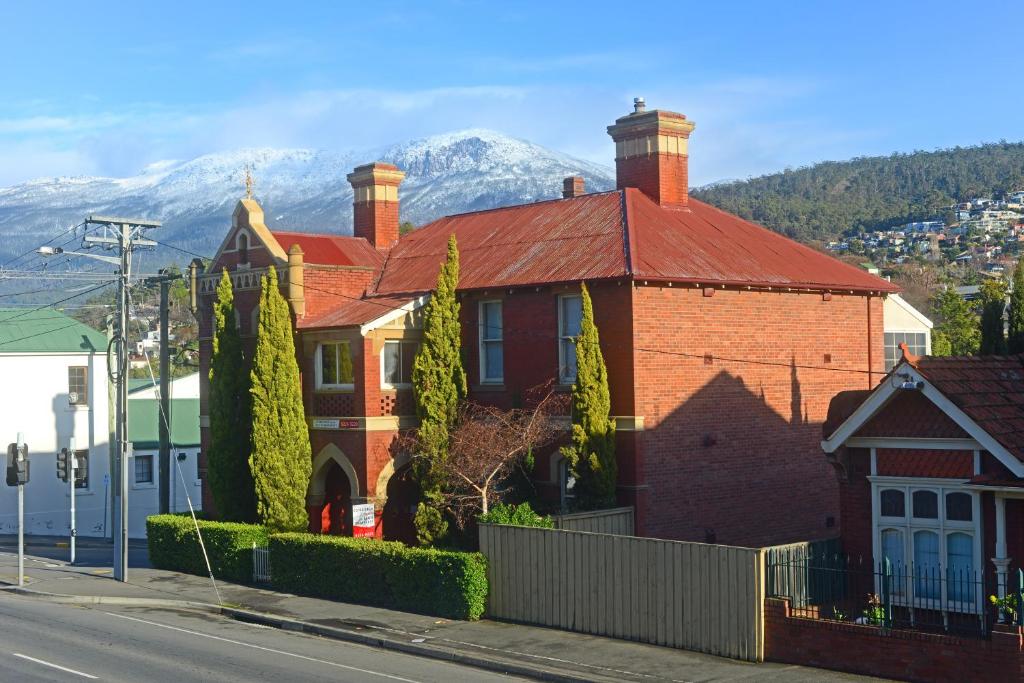 une maison en briques avec un toit rouge et des montagnes en arrière-plan dans l'établissement Edinburgh Gallery Bed & Breakfast, à Hobart