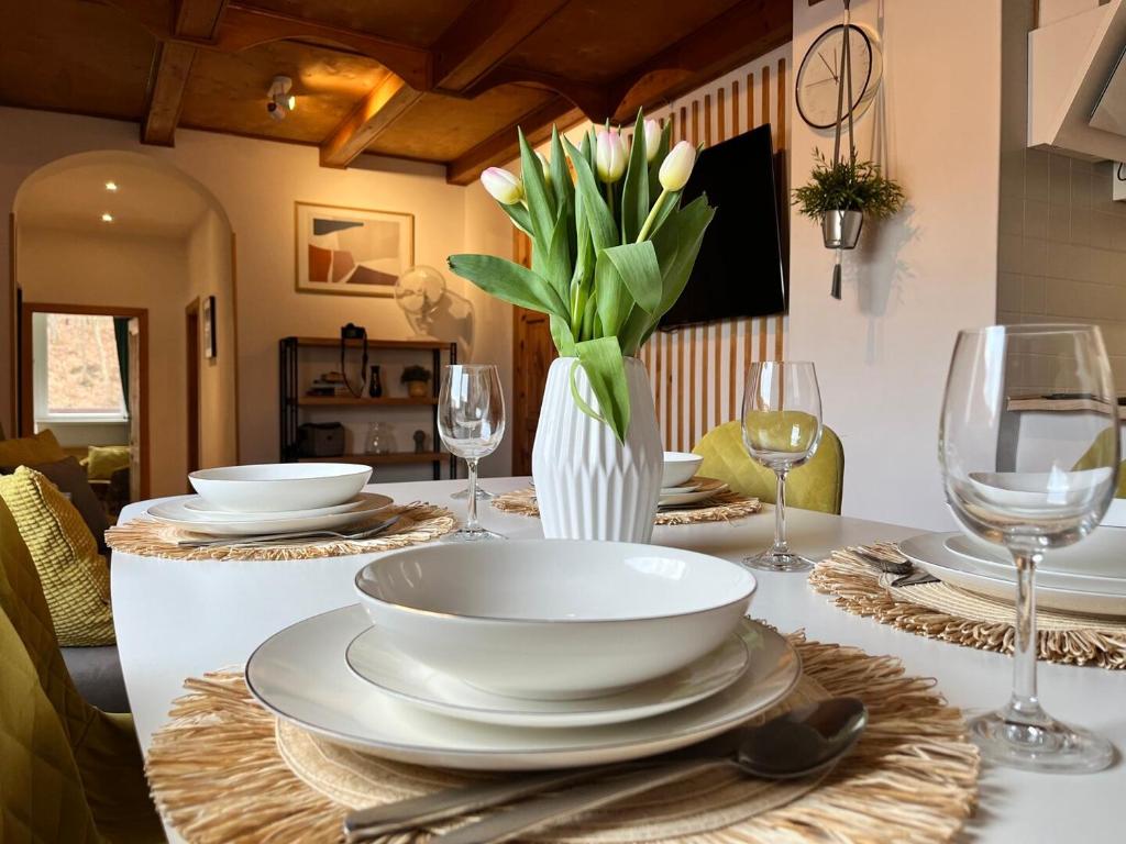 a table with plates and glasses and a vase of flowers at Spokojny Potok Sopot - AFRA GROUP in Sopot