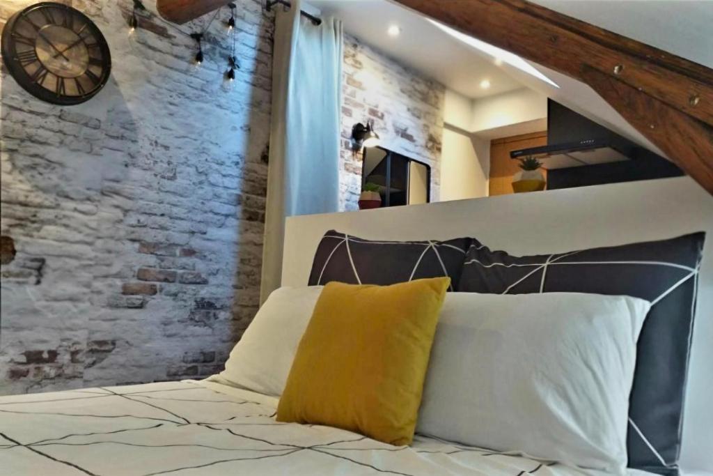 a bed with a clock on a brick wall at Cocon industriel pour Nuits étoilées in Bourges