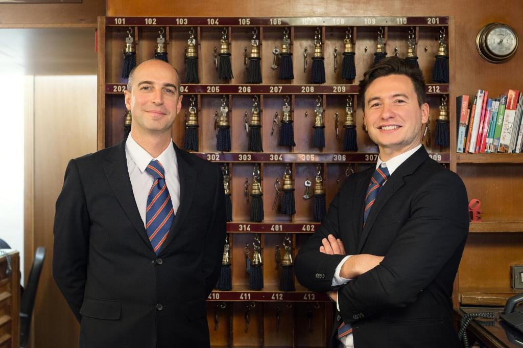 two men in suits standing in front of a shelf of wine bottles at Hotel Montecarlo in Venice