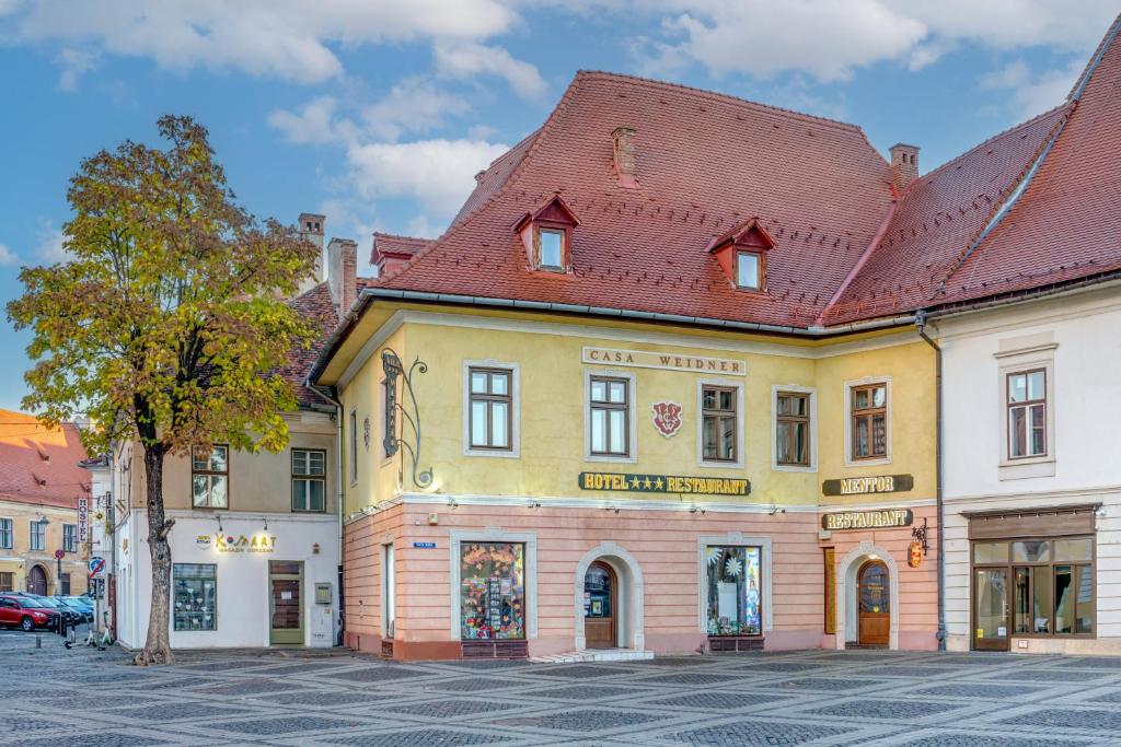 ein gelbes Gebäude mit rotem Dach an einer Straße in der Unterkunft Casa Weidner Hotel Sibiu in Sibiu