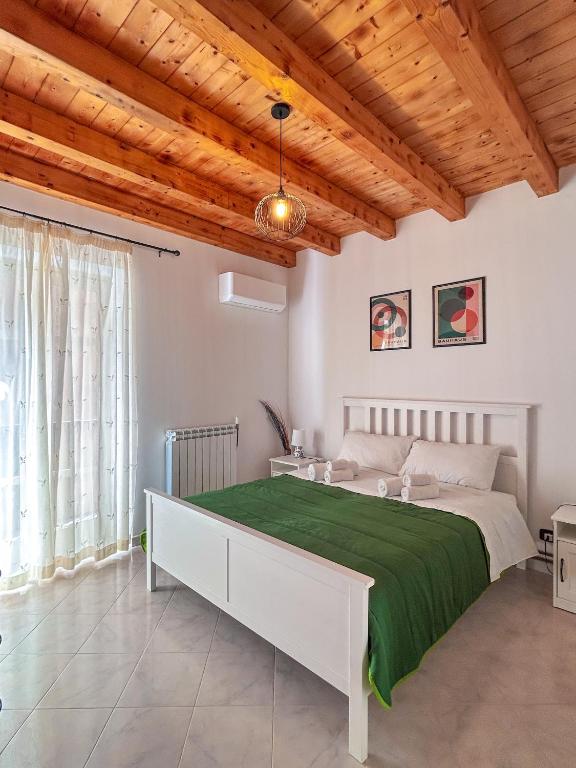 a white bedroom with a large bed with a green blanket at Casa Vacanza Nì Rosa in Cefalù