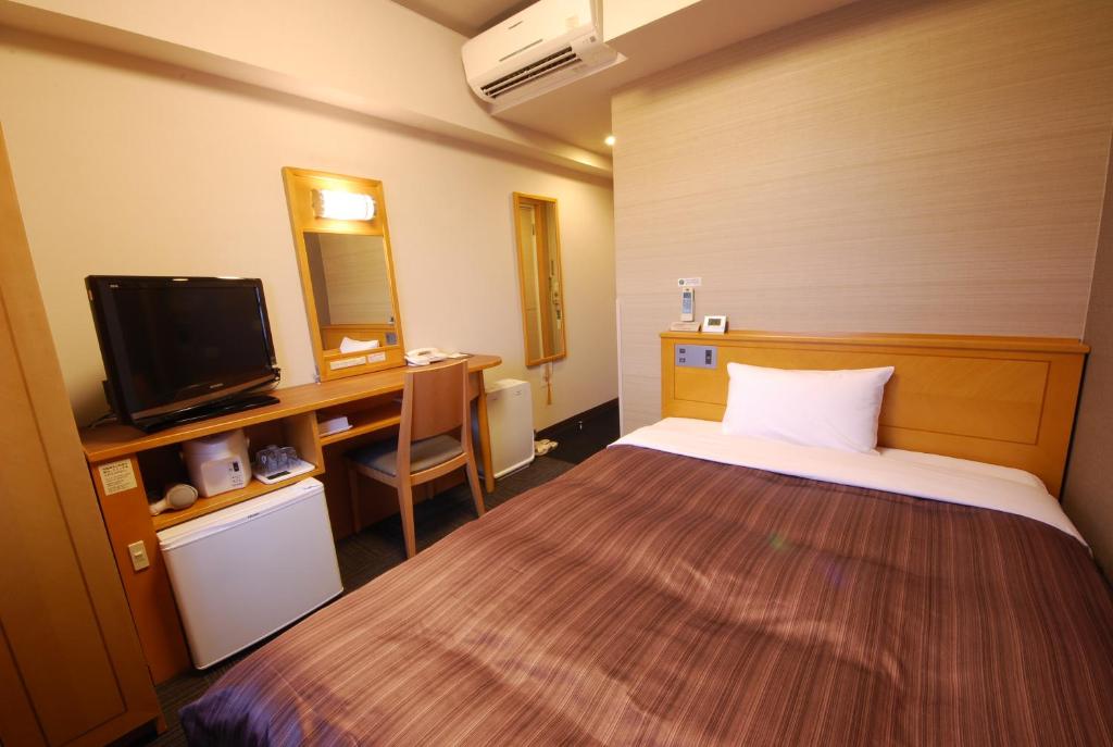 a room with a bed and a desk and a television at Hotel Route-Inn Hon Hachinohe Ekimae in Hachinohe