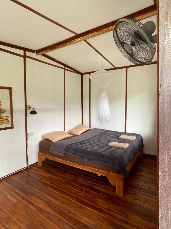 a bed in a room with a fan on the wall at Sapan Goodview สะปันกู๊ดวิว in Ban Na Luang