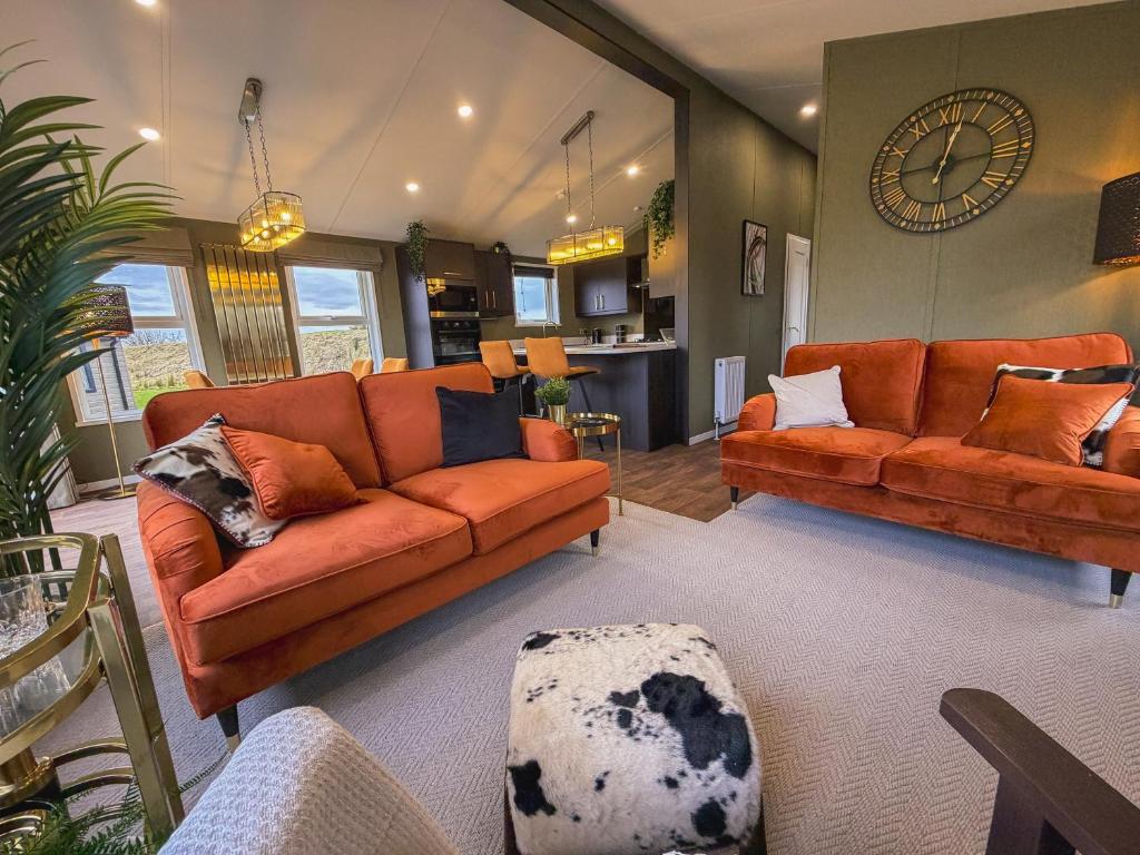 a living room with two orange couches and a clock at Honeysuckle Lodge in Bassenthwaite
