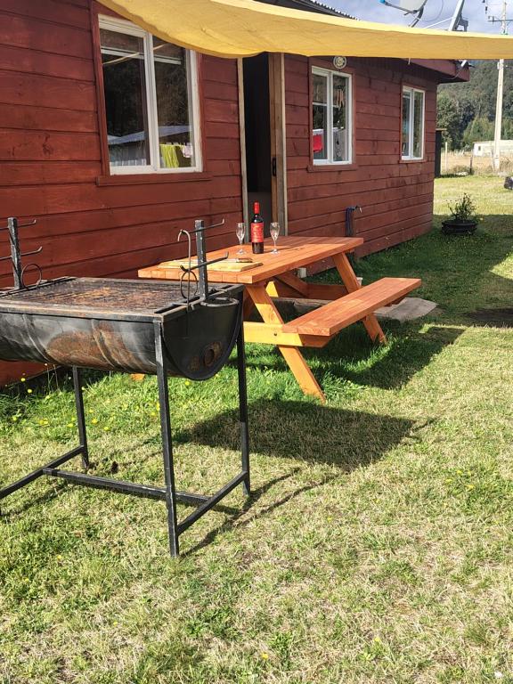 a picnic table with a grill in front of a house at Cabañas Entrelagos - Naturaleza , parrilla y tranquilidad cerca de Huilo -Huilo in Choshuenco