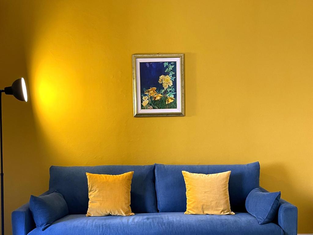 a blue couch against a yellow wall with a picture at Casa Obìa in Cagliari