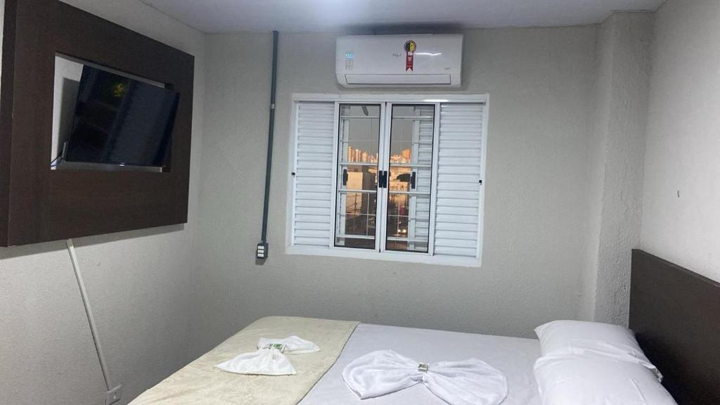 a bedroom with a bed with white sheets and a window at HotelItaveraMS in Campo Grande