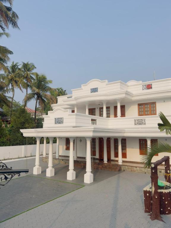 a large white building with columns and palm trees at Gem Palace in Perumpāvūr